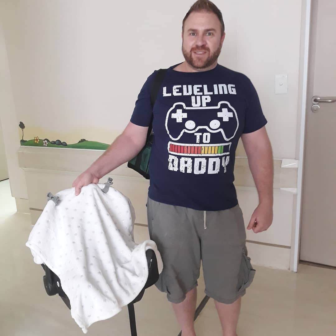 Warren in a 'Leveling Up to Daddy' T-shirt at the hospital with his newborn son's carrier