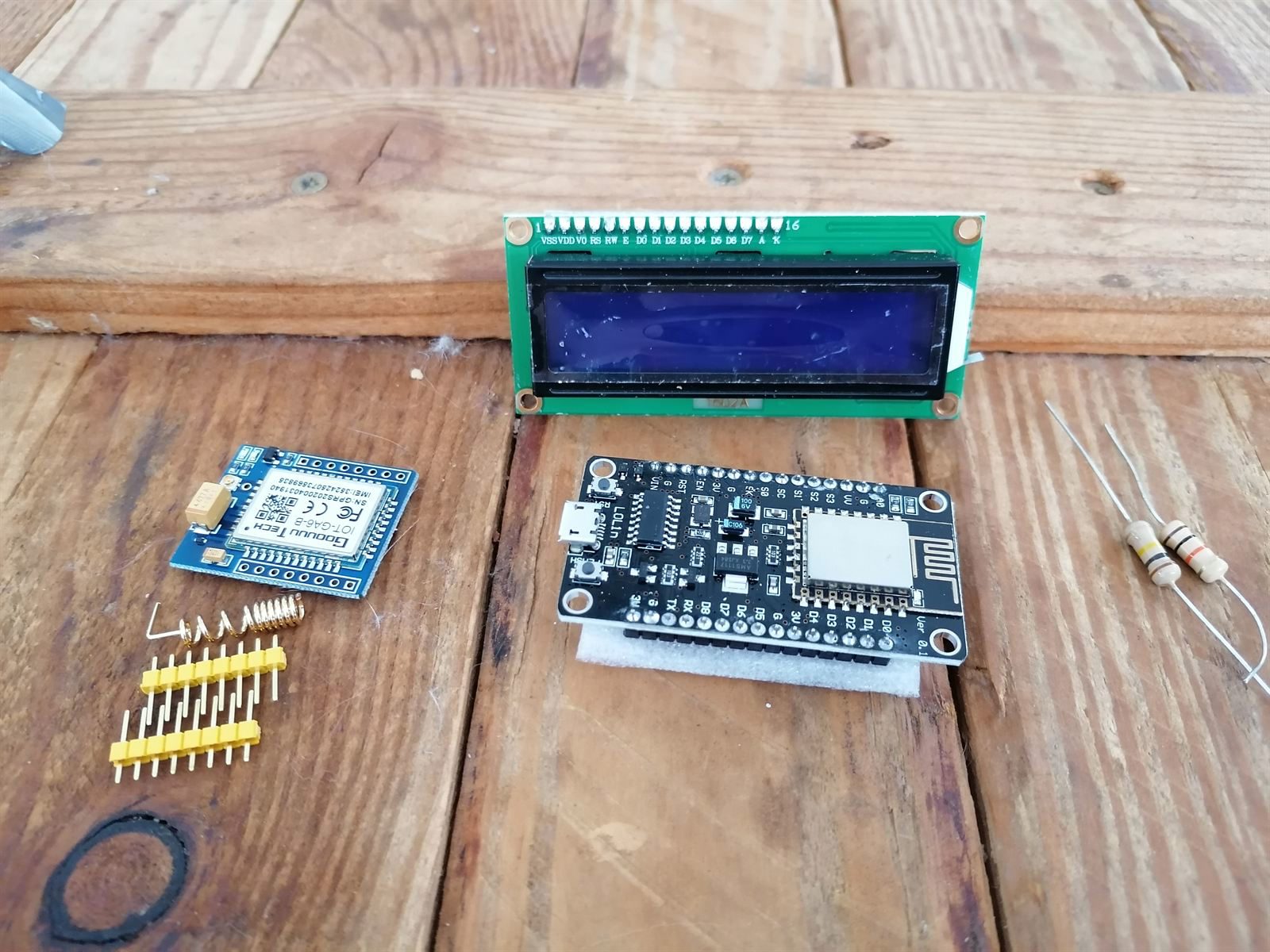 The starting parts laid out on pallet wood: LCD, microcontroller, cellular module, antennas, resistors