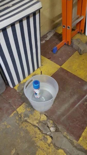 A spray can standing in a bucket of hot water on a garage floor