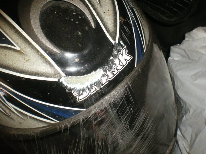 A motorcycle helmet with deep abrasion scarring ground across the chin bar and down one side, right through the paint