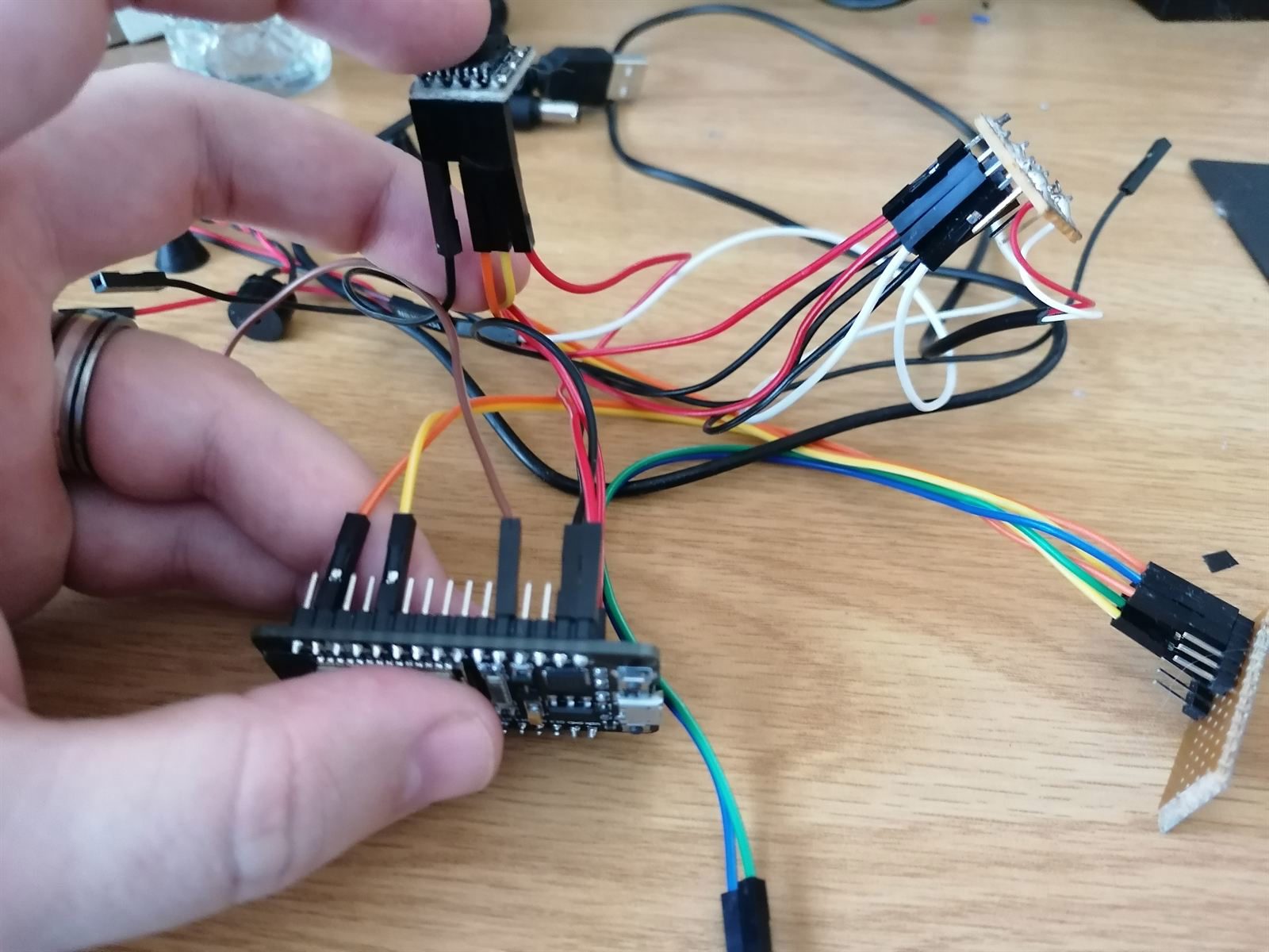 A hand holding a dev board buried in an absolute rat's nest of jumper wires