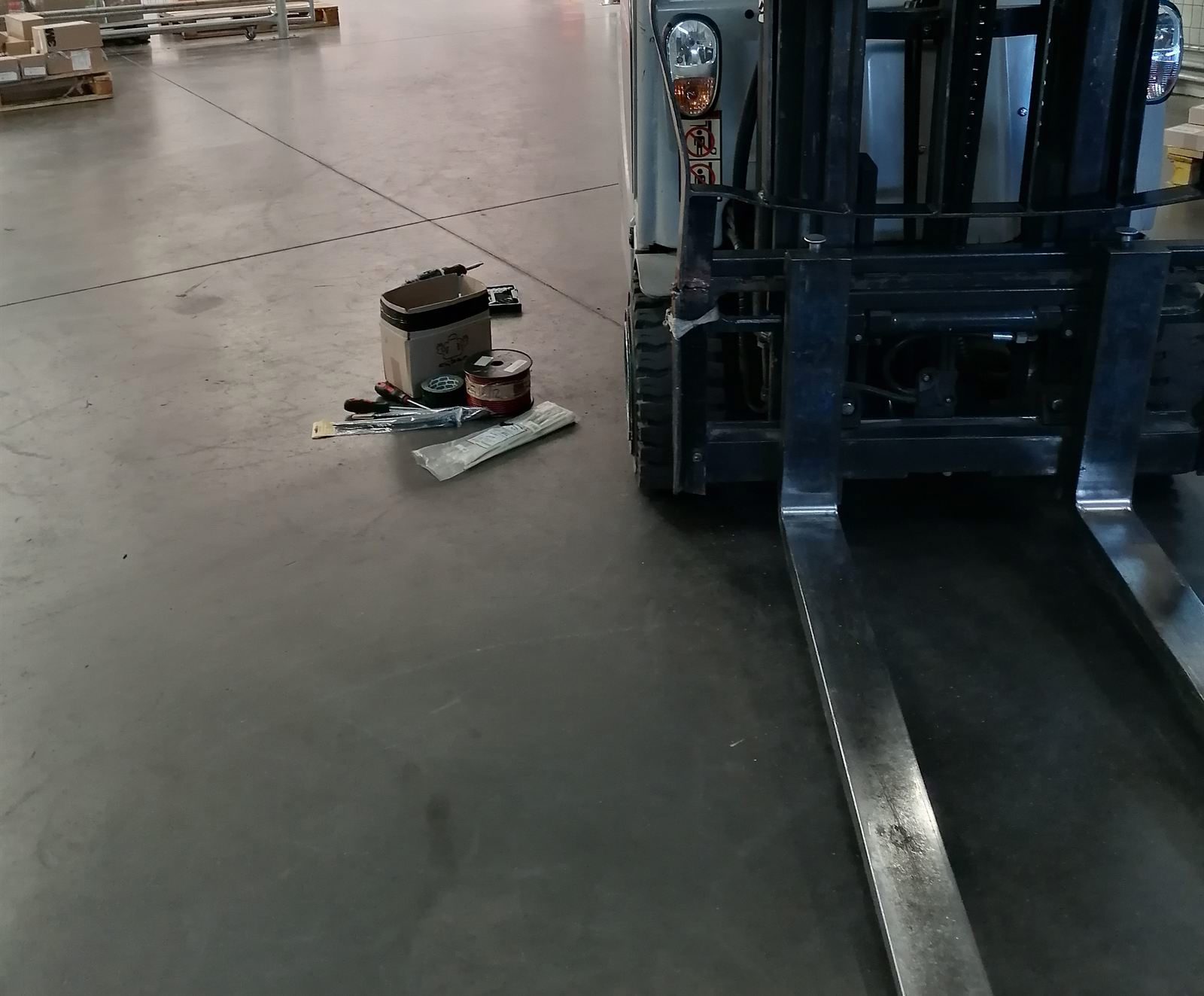 A forklift on the warehouse floor with tools and a component box laid out in front of it