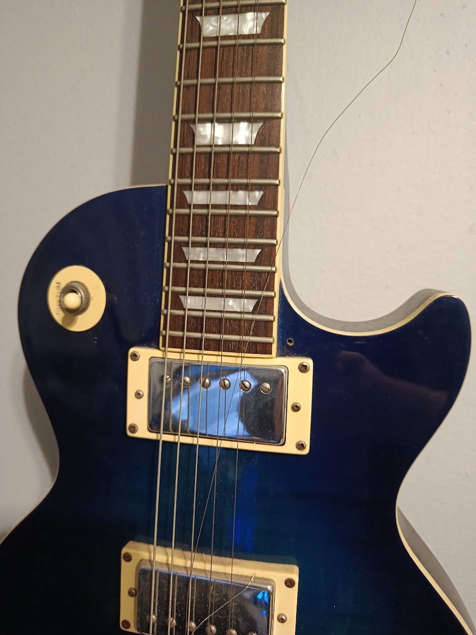 A blue electric guitar with a snapped string sprung loose off the fretboard, curling up and out of the top of the frame