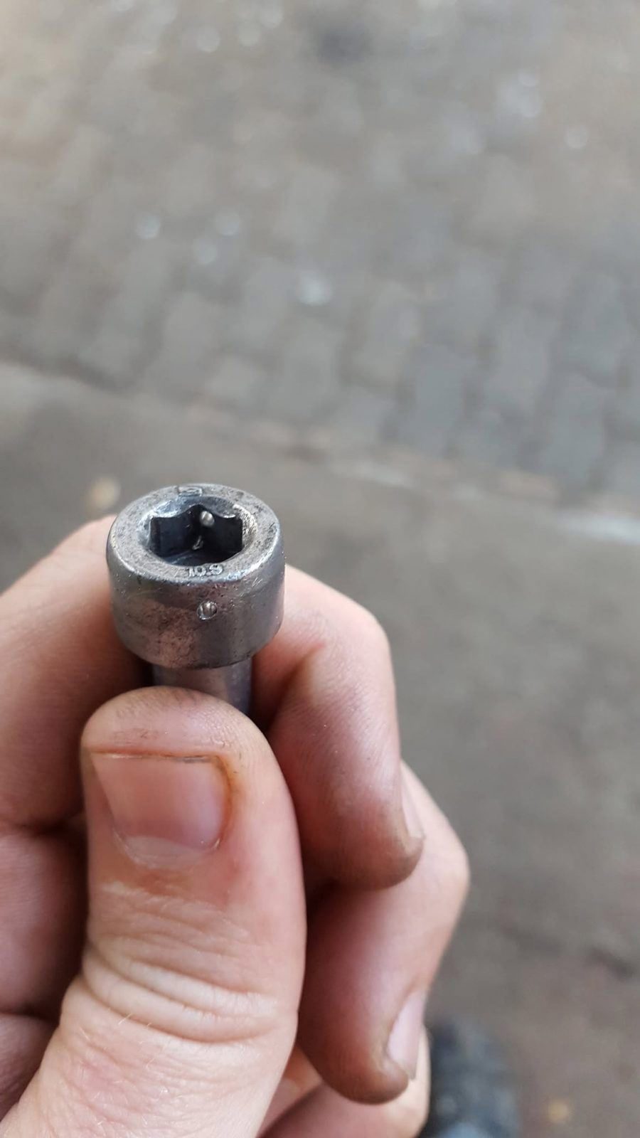 A drilled bolt head held between finger and thumb